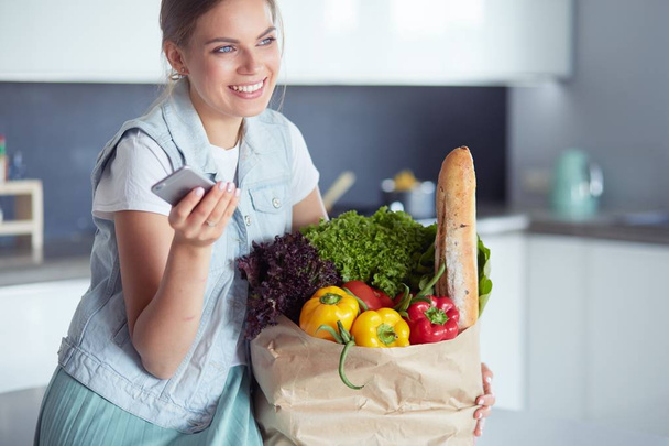 Молода жінка тримає продуктову торгову сумку з овочами.
 - Фото, зображення