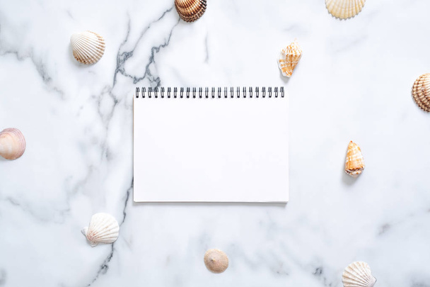 Sea shells and blank paper notepad with copy space for your text on marble background. Summer vacation concept. Flat lay, top view, overhead. - 写真・画像