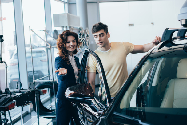 selektywne skupienie atrakcyjnego dealera samochodowego i przystojnego mężczyzny stojącego w pobliżu nowego samochodu - Zdjęcie, obraz