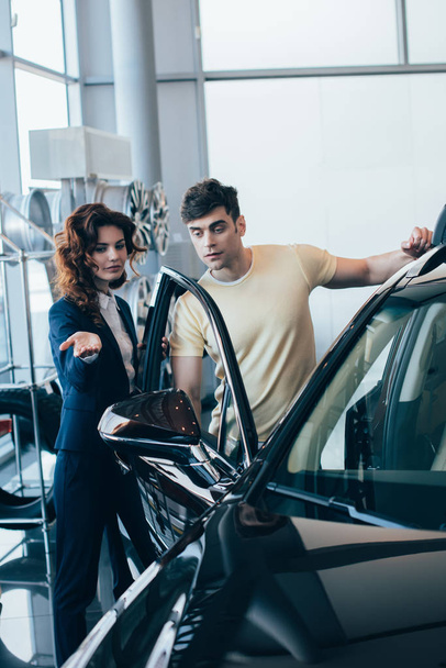 selective focus of attractive car dealer and handsome man standing near new car - Photo, Image
