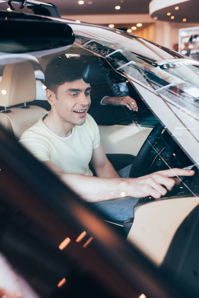 επιλεκτική εστίαση του ευτυχισμένο άνθρωπο που κάθεται σε νέο αυτοκίνητο και έμπορος αυτοκινήτων στέκεται κοντά στο παράθυρο του αυτοκινήτου - Φωτογραφία, εικόνα