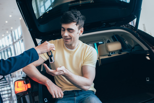 Teilansicht: Autohändler übergibt Autoschlüssel an glücklichen, gutaussehenden Mann - Foto, Bild