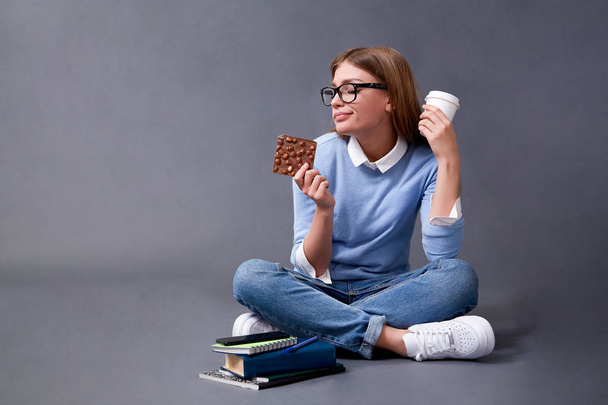 Student eating chocolate bar and drinking coffee. Student concept. Studio - Foto, Imagem