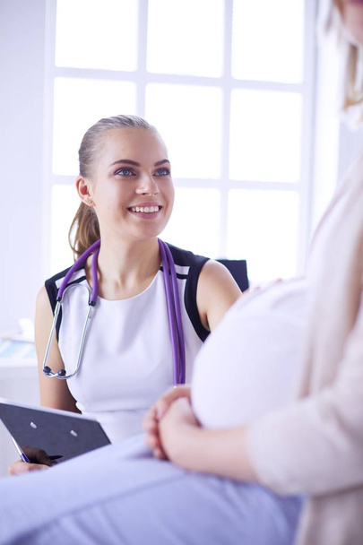 Young woman doctor with stethoscope and tablet speaking with pregnant woman at hospital. - 写真・画像