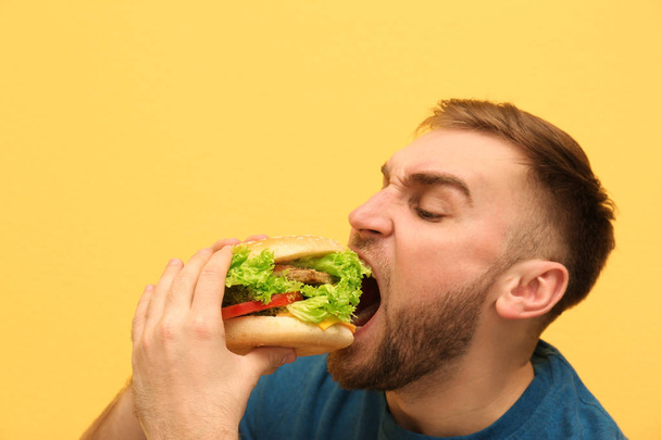 Young man eating tasty burger on color background. Space for text - Photo, image