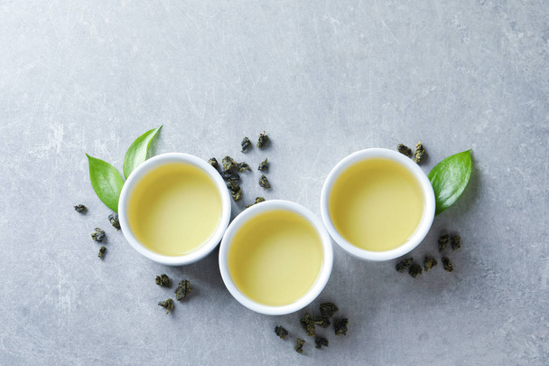 Cups of Tie Guan Yin oolong and tea leaves on grey background, top view with space for text - Foto, afbeelding
