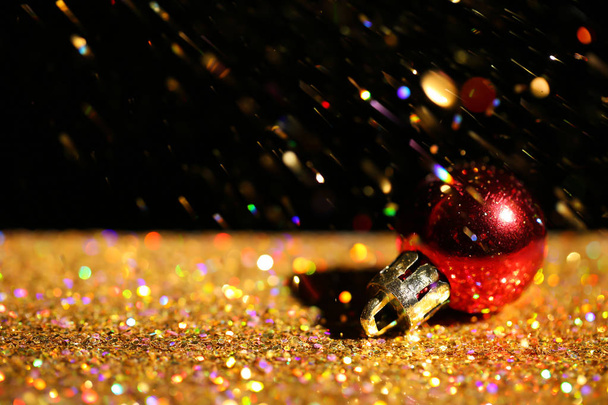 Golden paillettes and Christmas ball against black background. Space for text - Foto, Imagem