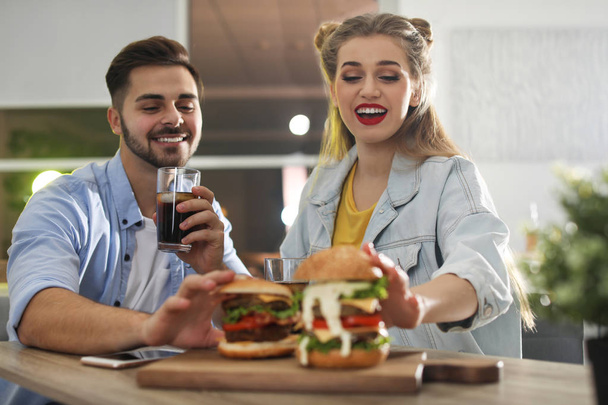 Happy young couple having lunch in burger restaurant - Φωτογραφία, εικόνα