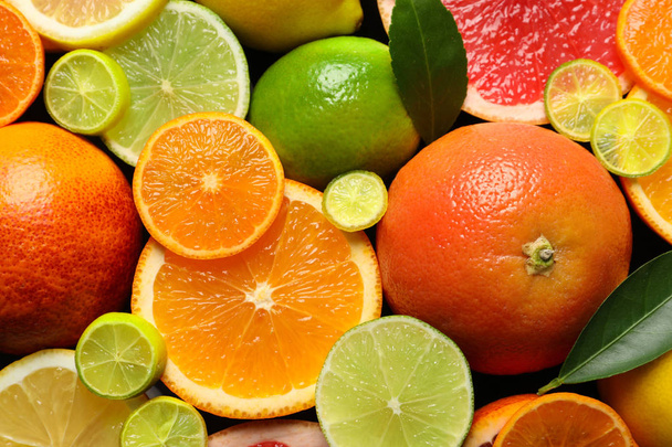 Sliced and whole citrus fruits with leaves as background, top view - Фото, изображение