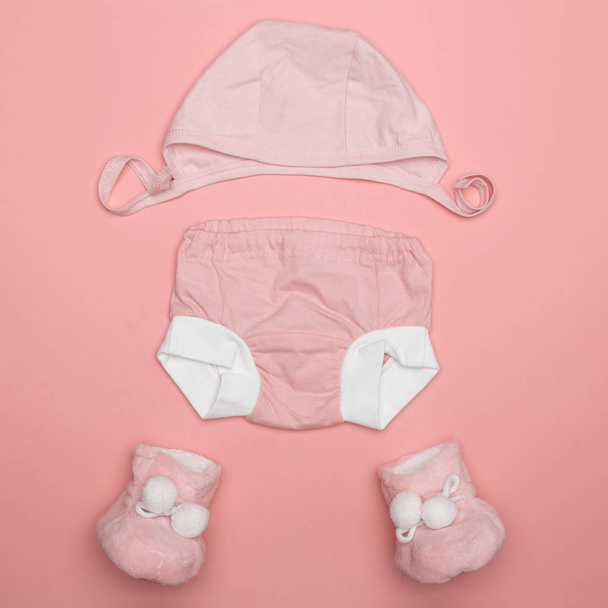 the layout in the pink color of children's things for newborns, hat, diaper, panties, slippers - Foto, afbeelding