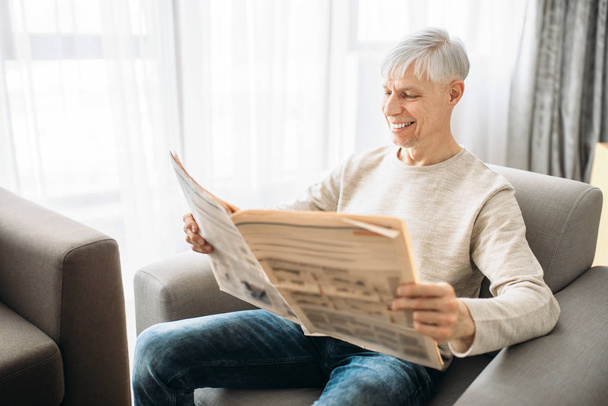 Hombre adulto sentado en el sofá y leyendo el periódico en casa. Hombre maduro se relaja en sillón
 - Foto, imagen