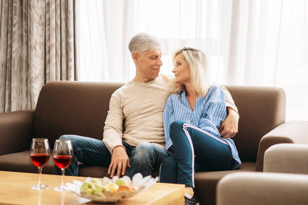 Romantic dinner of adult love couple at home. Mature husband and wife sitting on couch and embrancing, happy mature family - Photo, Image