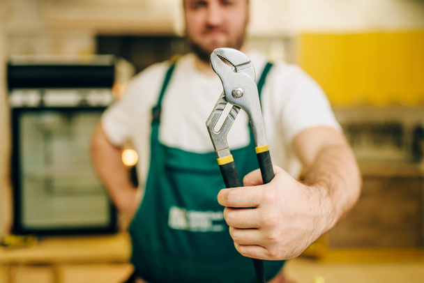 Repairman in uniform holds wrench, handyman. Professional worker makes repairs around the house, home repairing service - Foto, Imagen