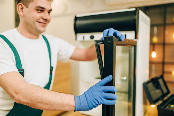 Pracownik w mundurze naprawy lodówki w domu. Naprawa pracy w lodówce, profesjonalna obsługa - Zdjęcie, obraz