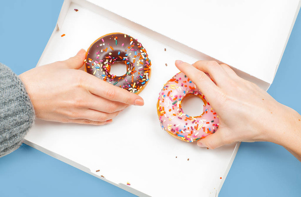 Female hands is taking two last donuts in box on pastel blue background.  - Fotoğraf, Görsel
