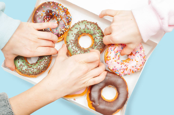 Many hands is taking donuts in box on blue background - Fotoğraf, Görsel