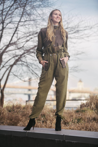 Fashionable smiling woman wearing long overalls outfit posing in the city - Zdjęcie, obraz