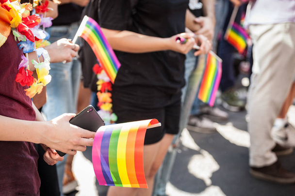Manos de una chica sosteniendo un teléfono inteligente con una cámara y una bandera gay arco iris durante un Orgullo Gay. La bandera del arco iris es uno de los símbolos de la comunidad LGBTQ
 - Foto, imagen