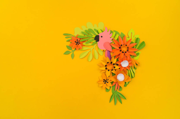 Decorative composition of tropical leaves and flowers. Paper craft. Yellow background. Pink parrot. - Фото, зображення