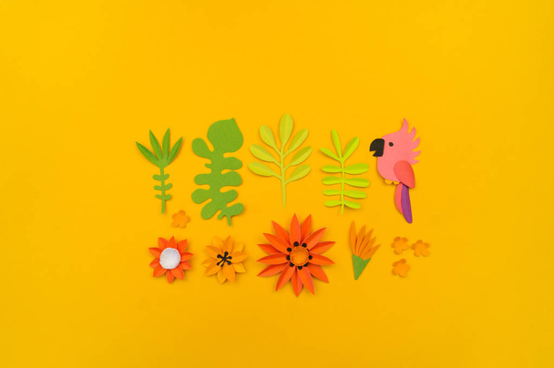 Decorative composition of tropical leaves and flowers. Paper craft. Yellow background. Pink parrot. - Фото, зображення