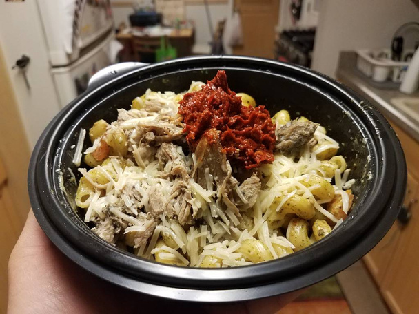 hand met bord pasta met kaas, varkensvlees en rode saus in keuken - Foto, afbeelding