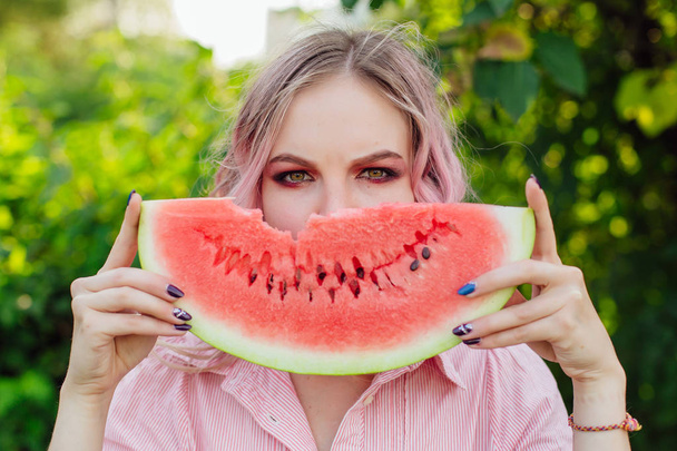 Beautiful young woman with pink hair holding juicy watermelon close to the face - Foto, afbeelding