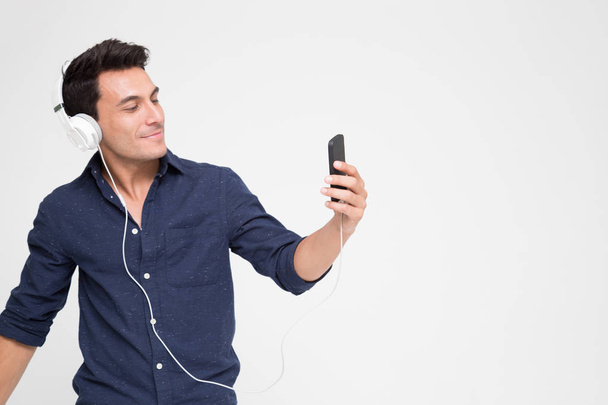 Handsome young Caucasian man listening music with headphones on smartphone, Teenager enjoying top chart music streaming service in website with his playlist on mobile - Foto, imagen