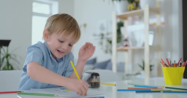 Uma criança pequena sentada à mesa desenha um desenho a lápis em cores diferentes
 - Filmagem, Vídeo