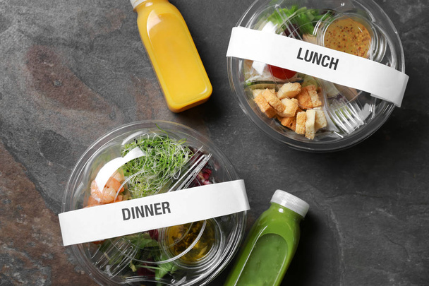 Behälter mit leckerem Essen und Saftflaschen auf grauem Hintergrund - Foto, Bild