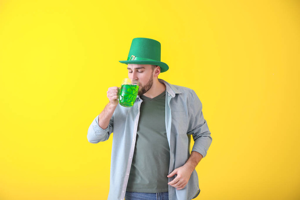 schöner junger Mann mit grünem Hut, der Bier auf farbigem Hintergrund trinkt. St. Patrick 's Day Feier - Foto, Bild