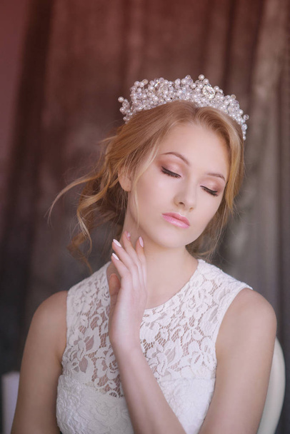Young beautiful bride with blond hair in a diadem and white veil and white dress - Фото, изображение
