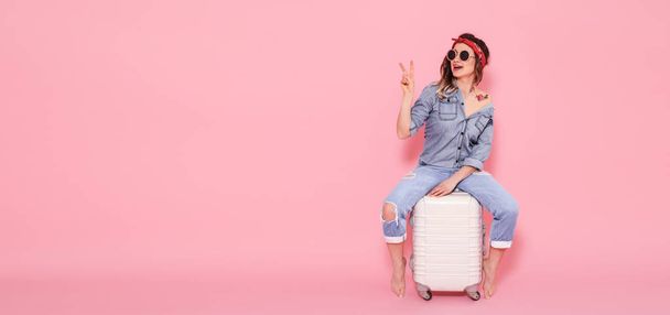 Красивая молодая девушка в джинсовой рубашке с наклейкой из цветов татуировки воды, улыбающаяся и сидящая на чемодане
 - Фото, изображение