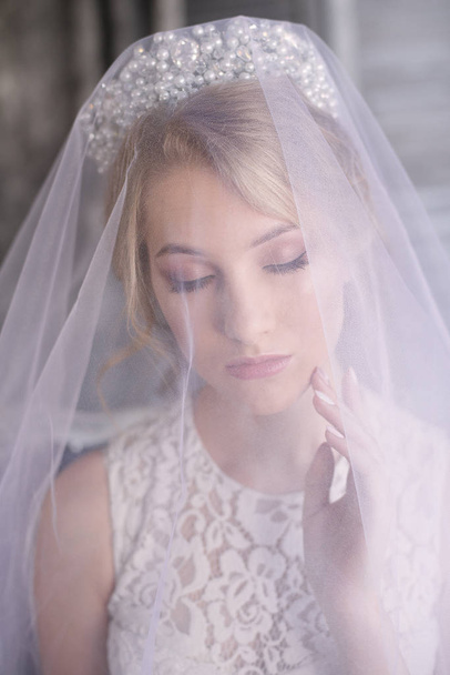 Young beautiful bride with blond hair in a diadem and white veil and white dress - Foto, Imagen