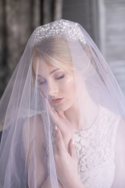 Young beautiful bride with blond hair in a diadem and white veil and white dress - Fotoğraf, Görsel