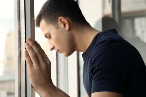 落ち込んで若い男の窓の近くに立っていると、自殺を考える - 写真・画像