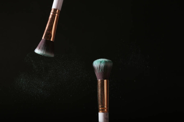 Make-up penselen en uitbarsting van eyeshadows op donkere achtergrond - Foto, afbeelding