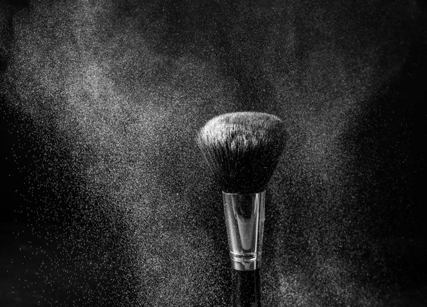 Cepillo de maquillaje y explosión de polvo sobre fondo oscuro
 - Foto, Imagen