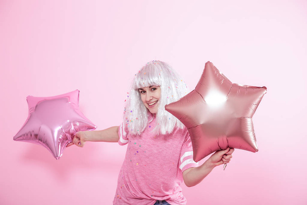 Funny Girl with silver hair gives a smile and emotion on pink background. Young woman or teen girl with balloons and confetti - Photo, Image
