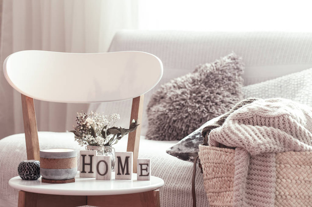 Velas, um vaso com flores com letras de madeira da casa na cadeira branca de madeira. Sofá e cesta de vime com almofadas no fundo
. - Foto, Imagem