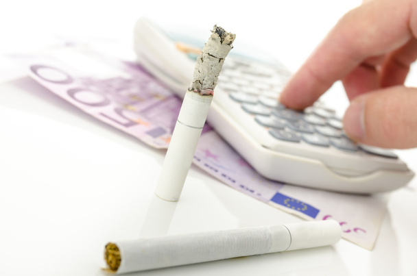 Cigarrillo medio quemado con calculadora y dinero en euros
 - Foto, Imagen