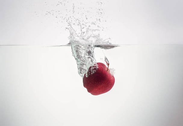apple falls into the water scattering a lot of splashes and drop - Photo, Image