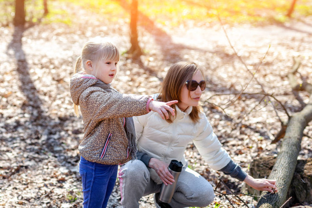Jonge volwassen moeder en dochtertje samen wandelen in het bos of park op een zonnige dag. Schattige blonde babymeisje wijzen met de vinger ergens - Foto, afbeelding