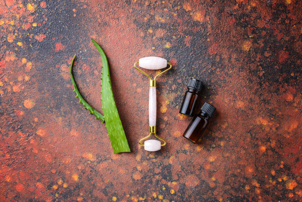 Gezichtsmassage tool met etherische olie en aloë vera op kleur achtergrond - Foto, afbeelding