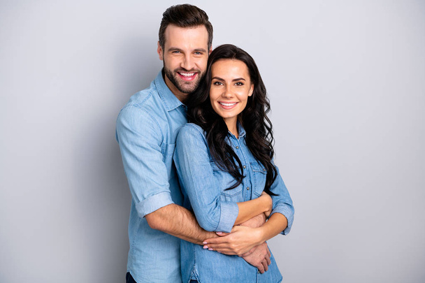 Joyful family. Portrait of isolated cute recently married people pregnant waiting for baby in warm sweet cuddles dressed in denim shirts over argent background - Foto, imagen