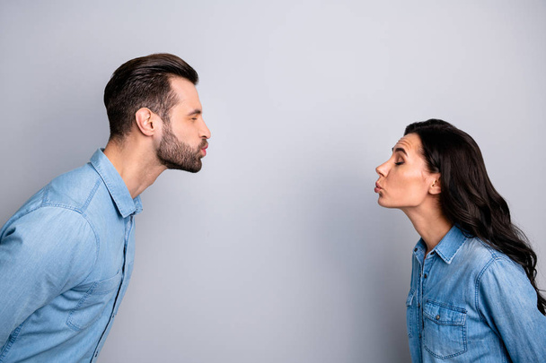 Blind dating. Profile side photo close up of cute funny shy spouses sending air kisses closing eyes showing feelings dressed in fashionable blue jackets isolated on ashy-gray background - Foto, afbeelding