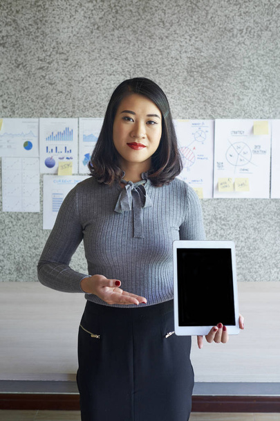 Πορτρέτο της Ασίας νεαρός επιχειρηματίας στέκεται και δείχνοντας ψηφιακή δισκίο με μαύρη κενή οθόνη στο γραφείο - Φωτογραφία, εικόνα
