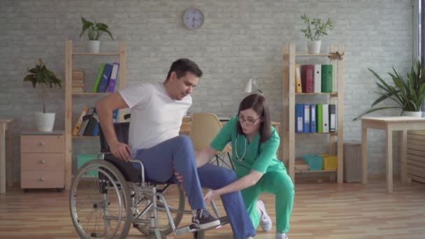 Girl nurse helps disabled person to get up from a wheelchair - Кадри, відео