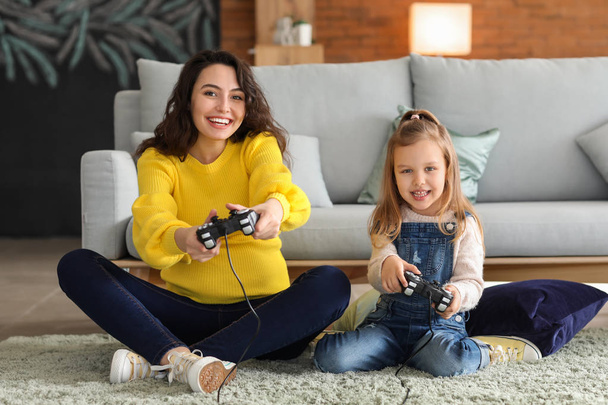 Беременная мать с маленькой дочерью, играющая в видеоигры дома
 - Фото, изображение