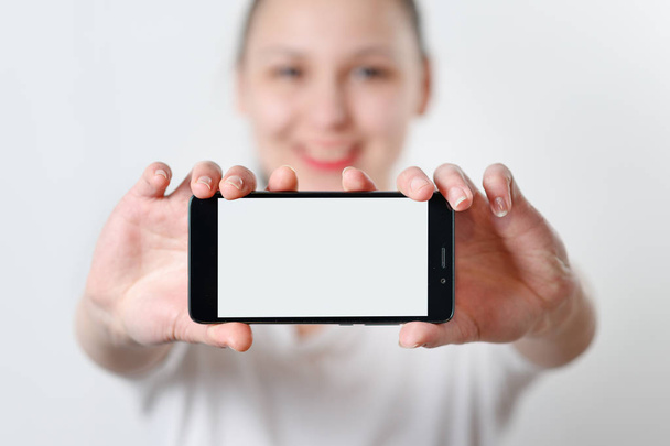 молода жінка тримає смартфон горизонтально з білим екраном з місцем для копіювання. на світлому фоні
 - Фото, зображення