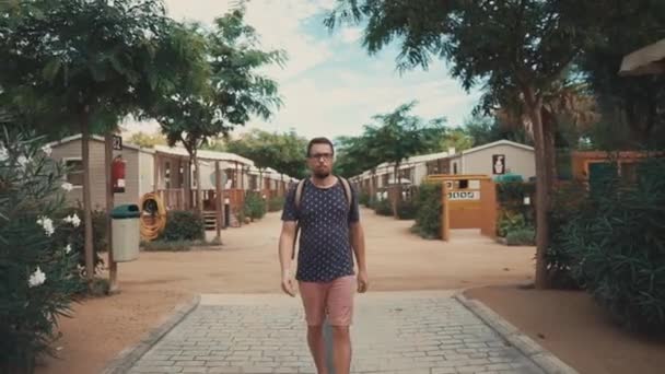 Parrakas turisti mies kävelee piha-alueella, jossa on pieniä kesämökkejä
 - Materiaali, video